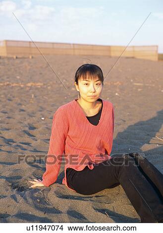 Picture - A young woman sitting on beach. Fotosearch