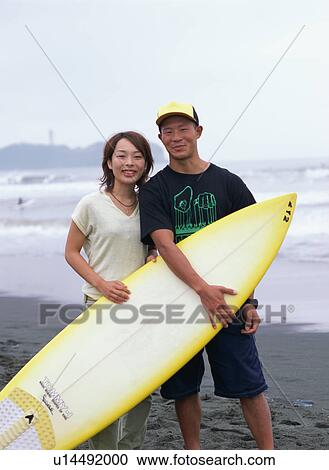 Stock Image - Young couple holding a surf board. Fotosearch