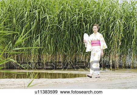 Stock Photo - A woman in kimono walking on lake side. Fotosearch