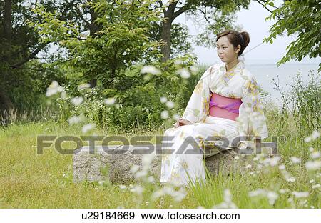 Stock Photo - A young woman in kimono sitting outside. Fotosearch