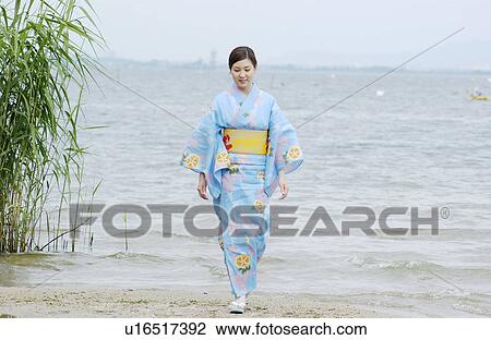 Stock Image - A young woman in kimono walking on lake side. Fotosearch