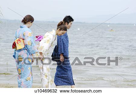 Stock Image - Three people in kimono standing on lake side. Fotosearch