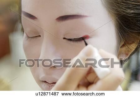 Stock Photo - A Geisha woman applying makeup. Fotosearch