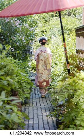 Stock Image - A Geisha woman walking on a street, rear view. Fotosearch