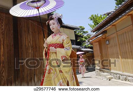 Stock Photograph - Two Geisha women with umbrella walking on a street. Fotosearch