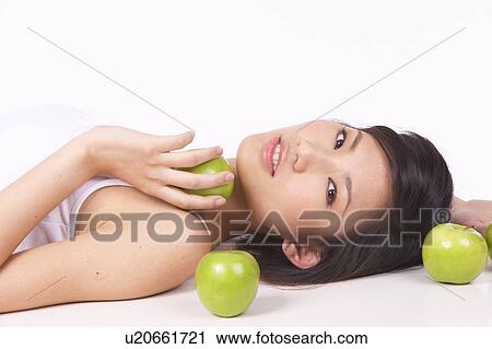 Stock Image - Portrait of Natural Young girl lying on Floor, Holding Apple. Fotosearch