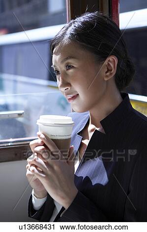 Stock Image - Young Businesswoman Riding Tram, Holding Coffee Cup, Looking Away, Smiling. Fotosearch