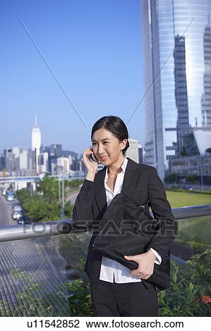 Stock Image - Young Businesswoman Standing in Street, Using Mobile Phone, Smiling. Fotosearch