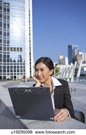 Stock Photo - Young Businesswoman using Laptop Outdoor, Looking Away. Fotosearch
