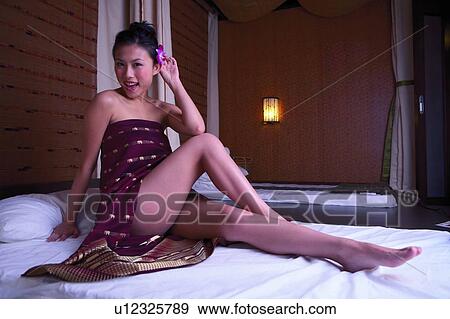 Stock Photo - Young womain sitting in spa room, holding flower, full length. Fotosearch