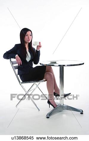 Stock Photography - Young woman in business suit, relaxing on chair and holding a cup, full length. Fotosearch