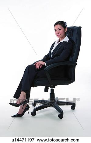 Stock Photo - Young woman in business suit, sitting on armchair, side view. Fotosearch