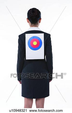 Stock Image - Young woman in business suit, standing, wearing a target on back, rear view. Fotosearch