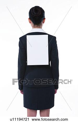 Stock Image - Young woman in business suit, standing, wearing a blank paper on back, rear view. Fotosearch