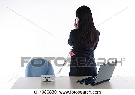 Stock Image - Young woman in business suit, standing, talking over the phone, rear view. Fotosearch
