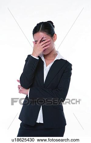 Stock Image - Young woman in business suit, standing, hand covering eyes and thinking. Fotosearch
