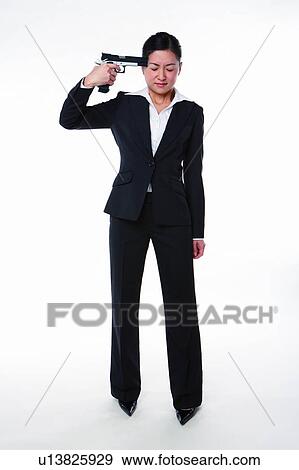 Stock Photo - Young woman in business suit, standing with gun pointing to head, full length. Fotosearch