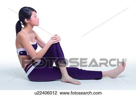 Stock Image - Young woman sitting on floor, meditating. Fotosearch
