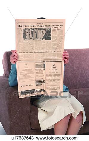 Stock Image - Young woman sitting on sofa and reading newspaper. Fotosearch