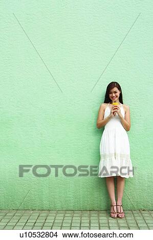 Picture - Young woman standing, holding glass of orange juice, full length. Fotosearch