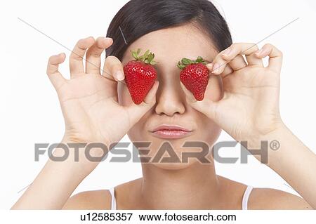 Stock Photo - Portrait of Natural Young girl holding two Strawberries on eyes. Fotosearch