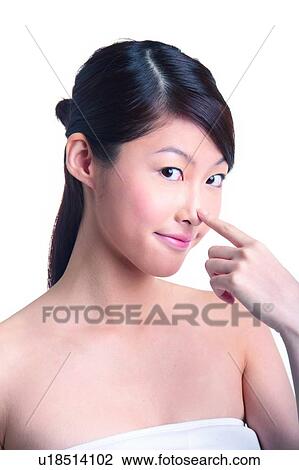 Stock Image - Young woman standing with finger on nose. Fotosearch