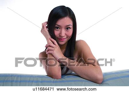 Stock Image - Young woman with long hair, smiling, leaning on sofa. Fotosearch