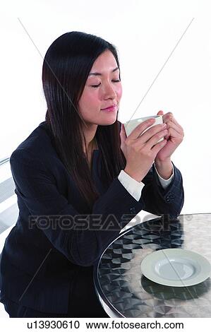 Stock Image - Young woman in business suit, holding cup with both hands, eyes closed. Fotosearch