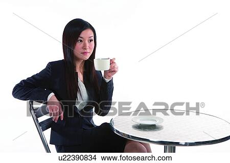 Picture - Young woman in business suit, relaxing on chair and holding a cup. Fotosearch
