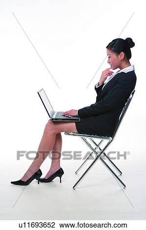 Stock Image - Young woman in business suit, sitting, using laptop, side view. Fotosearch