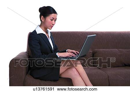 Stock Image - Young woman in business suit, sitting on sofa, using Laptop, close-up. Fotosearch