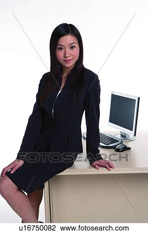 Young woman in business suit, sitting on table, looking at camera View Large Photo Image Stock Image - Young woman in business suit, sitting on table, looking at camera. Fotosearch