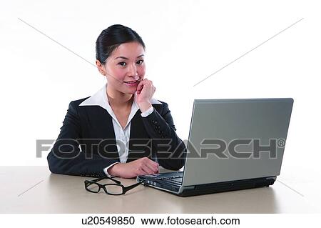 Stock Image - Young woman in business suit, sitting, using laptop. Fotosearch