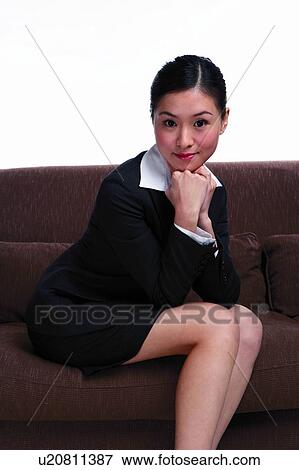 Young woman in business suit, sitting on sofa, looking at camera View Large Photo Image Stock Photo - Young woman in business suit, sitting on sofa, looking at camera. Fotosearch