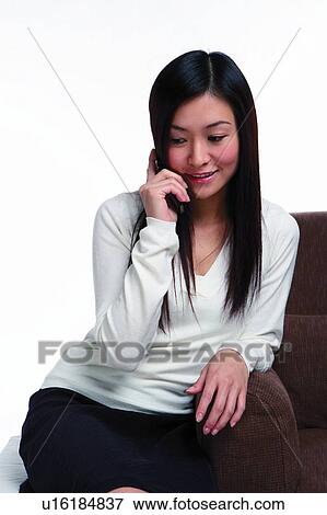 Stock Photo - Young woman leaning against sofa, using mobile phone. Fotosearch