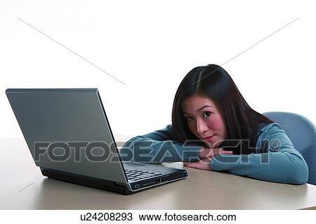 Stock Image - Young woman leaning on table with hands supporting the chin. Fotosearch