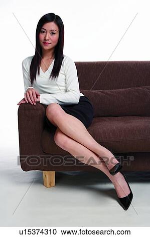 Stock Image - Young woman leaning to sofa, looking at camera, smiling. Fotosearch