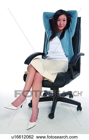 Stock Image - Young woman relaxing on armchair with hands folding behind the head. Fotosearch