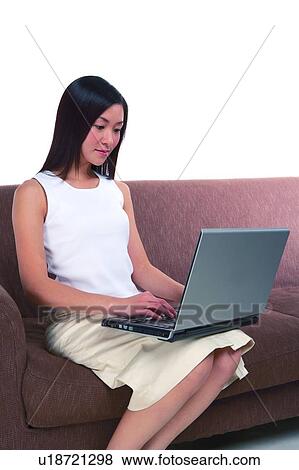 Stock Photo - Young woman sitting on sofa and looking at laptop. Fotosearch