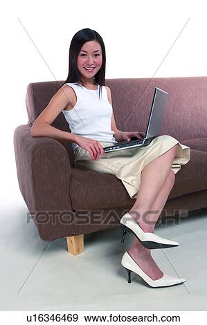 Young woman sitting on sofa and putting computers on thigh View Large Photo Image Stock Photo - Young woman sitting on sofa and putting computers on thigh. Fotosearch