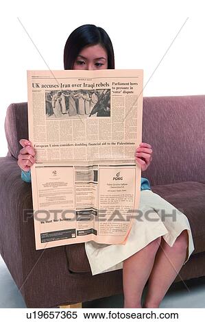 Stock Photography - Young woman sitting on sofa and reading newspaper. Fotosearch