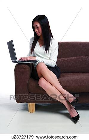 Young woman sitting on sofa, using laptop View Large Photo Image Stock Photo - Young woman sitting on sofa, using laptop. Fotosearch