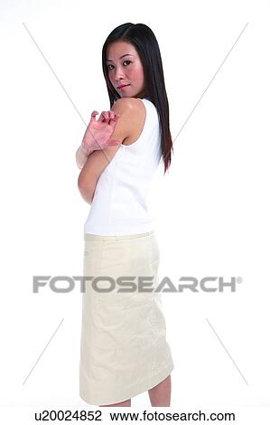 Stock Image - Young woman standing, turning back and in a gesture of holding something, three quarter length. Fotosearch