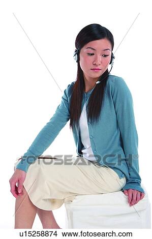 Picture - Young woman wearing headphone, looking down and thinking, three quarter length. Fotosearch