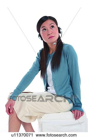 Stock Image - Young woman wearing headphone, looking up and thinking, three quarter length. Fotosearch