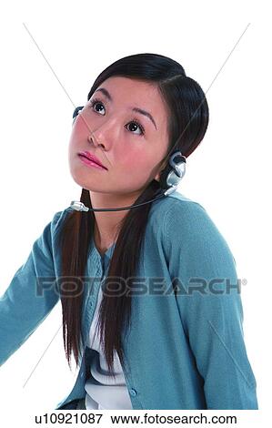 Stock Photo - Young woman wearing headphone, looking up and thinking. Fotosearch
