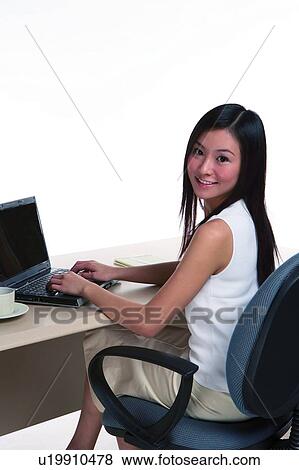 Stock Photo - Young woman working, looking back, in office environment. Fotosearch