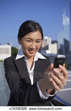 Stock Photograph - Young Businesswoman Looking at Mobile Phone, Smiling. Fotosearch