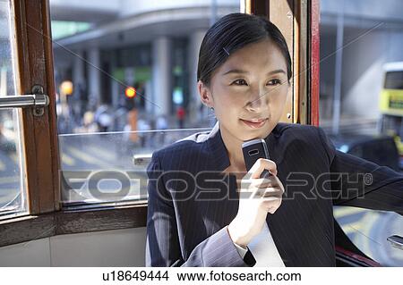 Young Businesswoman Riding Tram, Holding Mobile Phone, Smiling, Looking Away View Large Photo Image Picture - Young Businesswoman Riding Tram, Holding Mobile Phone, Smiling, Looking Away. Fotosearch