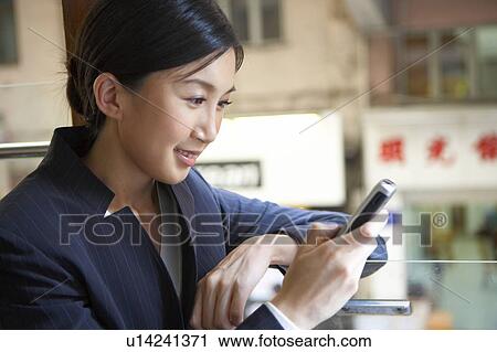 Stock Image - Young Businesswoman Riding Tram, Looking at Mobile Phone, Smiling. Fotosearch